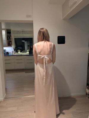 Ljusrosa långklänning med öppen rygg - Säljer nu min bakklänning i rosa satin med v-ringning och öppen rygg. Klänningen har smala axelband och knytning i ryggen för en snygg detalj. Köpt på Jj’s house. Jag har vanligtvis storlek S och denna passar perfekt. 