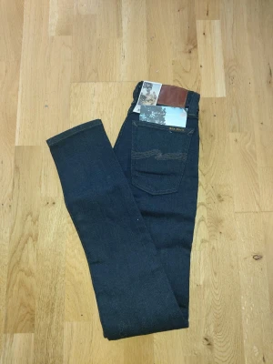 Mörkblå jeans från Nudie Jeans Co - Snygga mörkblå jeans från Nudie Jeans Co i klassisk rak modell. Jeansen har fem fickor, kontrastsömmar och läderpatch bak i midjan. Tillverkade i 100% bomull för en autentisk denimkänsla.