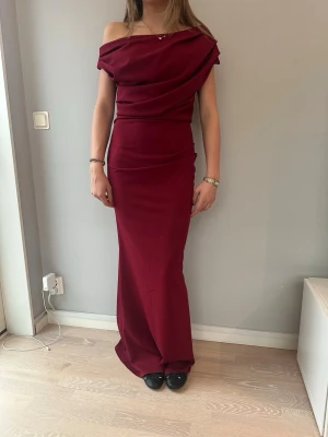 Vinröd offshoulder långklänning, balklänning  - Säljer en elegant vinröd långklänning med offshoulder-design och draperad överdel. Klänningen har en figurnära passform och är perfekt för speciella tillfällen. Perfekt för en bal eller andra speciella tillfällen. Materialet känns mjukt och följsamt mot kroppen. Klänningen är helt ny och är i storlek S. 