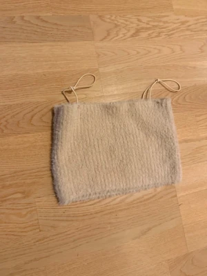Beige stickad bandeau topp - Mysig beige bandeau topp med tunna axelband och stickad struktur. Perfekt för att skapa en trendig lager-på-lager-look eller bära som den är under varmare dagar.