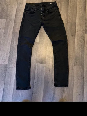Svarta slim fit jeans med knappar - Svarta slim fit jeans med knappgylf och klassiska fem fickor. Jeansen har en stilren look och smal passform som sitter snyggt på benen. Perfekta för dig som gillar en enkel men trendig stil.