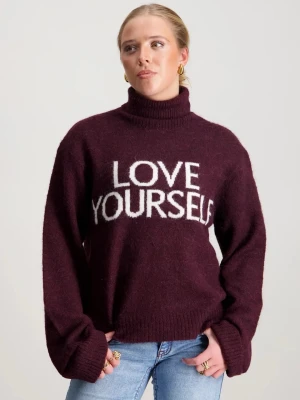Vinröd stickad tröja med text - Säljer en vinröd stickad tröja med hög krage och vit text 'LOVE YOURSELF' på bröstet. Tröjan har långa ärmar och ribbstickade muddar vid ärmslut och nederkant. Perfekt för att göra ett statement och hålla sig varm. Använd enstaka gång!!!