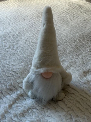 Vit tomtefigur med lång luva - Söt tomtefigur i mjukt material med lång, vit luva och fluffigt vitt skägg. Tomten har en rund,  näsa och små ben och armar. Perfekt som dekoration till vintern eller julen.