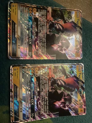 Pokémonkort Tapu Koko GX big size/XL - Två stycken Pokémonkort av typen Tapu Koko GX med holografisk yta. Korten har färgstarka motiv i svart, gult och lila med detaljer i silver och regnbågsfärger. Text och symboler i guld och vitt. Perfekt för samlare eller Pokémon-fans. 2 st big size tapu koko Ink. Båda två