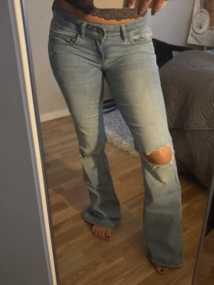 Ljusblå bootcut jeans med slitningar - Säljer ett par ljusblå bootcut jeans med slitningar på knäna och klassiska fem fickor, som tyvärr inte kommer till användning längre. Jeansen har låg midja och en snygg, avslappnad passform. Perfekta för dig som gillar en trendig och avslappnad stil.