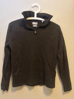 Mörkbrun stickad tröja med halvzip - Mysig mörkbrun stickad tröja från These Glory Days med halvzip framtill. Tröjan har lång ärm och hög krage, perfekt för lager-på-lager. Materialet känns mjukt och passar bra till både jeans och chinos.