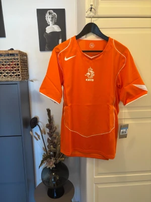 Orange KNVB fotbollströja Nike 2004 reissue  - Säljer en orange fotbollströja från Nike med KNVB-logga på bröstet. Tröjan har vita detaljer och är tillverkad i lätt och ventilerande material, perfekt för träning eller match. Klassisk v-ringning och korta ärmar.