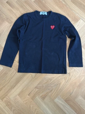 Svart långärmad T-shirt Comme des Garçons - Svart långärmad topp från Comme des Garçons PLAY med det ikoniska röda hjärte-logotypen broderad på bröstet. Tillverkad i mjuk bomull och har en klassisk, normal passform. Perfekt till jeans eller kjol för en clean look. Står M men passar dig som är S eller XS eftersom det är japansk storlek 👍