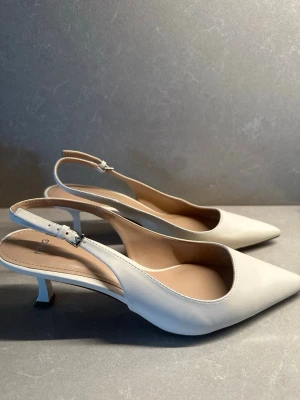 Vita Mango klackar  - Eleganta vita Mango klackar med spetsig tå och smal klack. Perfekta till fest, bröllop, examen eller sommarens finare tillfällen.  Skorna är använda men i fint skick – se bilder för mindre slitage under sulan och en liten märken framtill. Bekväma och stilrena med justerbar rem bak.   ✨ Tidlös modell ✨ Lättmatchade ✨ Klack 7cm 