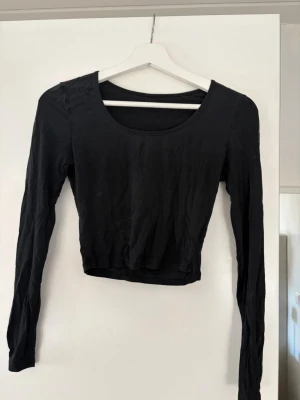 Svart croppad långärmad topp - En svart croppad topp med lång ärm och rund halsringning. Enkel och stilren design som passar perfekt till jeans eller kjol. Mjuk och stretchig känsla.