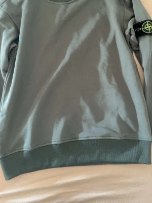 Grön sweatshirt från Stone Island - Snygg grön sweatshirt från Stone Island med klassisk logotyp-patch på ärmen. Tröjan har rund halsringning och ribbade muddar vid ärmslut och nederkant. Perfekt för en avslappnad och trendig stil. Stl S