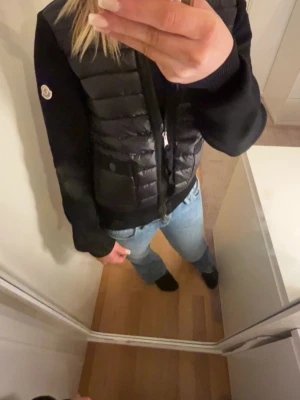 Svart hybridjacka från Moncler - Snygg svart hybridjacka från Moncler med quiltad, glansig front i dun och ärmar samt rygg i mjuk bomull. Jackan har dragkedja framtill och Moncler-logga på ärmen. Perfekt för lager-på-lager och streetstyle. Skriv om du vill ha fler videos. Scannen funkar och ahr även lappar så skriv om du är intresserad!!PRIS KAN DISKUTERAS!!!