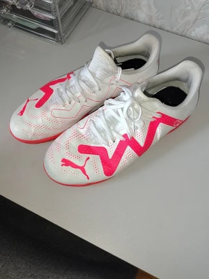 Vita och rosa fotbollsskor från Puma - Snygga fotbollsskor från Puma i vitt med starka rosa detaljer och logga. Skorna har snörning, låg profil, inomhus skor, utan dubbar . 