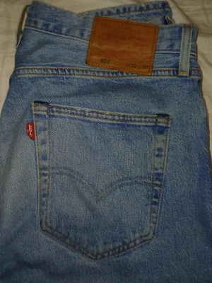 Levi's 501 ljusblå jeans W32 L30 - Klassiska ljusblå Levi's 501 jeans i rak modell med fem fickor och knappgylf. Tillverkade i slitstark bomull med den ikoniska röda Levi's-lappen på bakfickan och läderpatch i midjan. Perfekta för en avslappnad och tidlös stil.