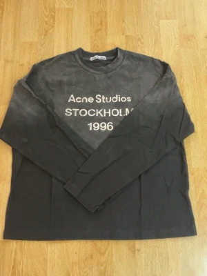 Svart långärmad topp Acne Studios - Cool svart långärmad topp från Acne Studios med tryck 'Acne Studios STOCKHOLM 1996' på bröstet. Klassisk rund halsringning och relaxed fit. Perfekt till jeans eller kjol för en avslappnad look.