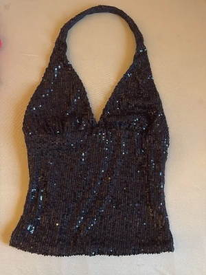 Marinblå paljettopp från Bershka - Supersnygg marinblå halterneck topp från Bershka med glittriga paljetter över hela. Toppen har djup v-ringning och är figurnära med en croppad passform. Perfekt för dig som vill sticka ut och glänsa lite extra.