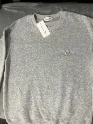 CD sweatshirt - Snygg grå sweatshirt med en logga på bröstet. Klassisk rund halsringning och ribbade muddar vid ärmslut och nederkant. Perfekt för en clean och stilren look skickas inom 24 timmar passar för dig mellan 175-180cm