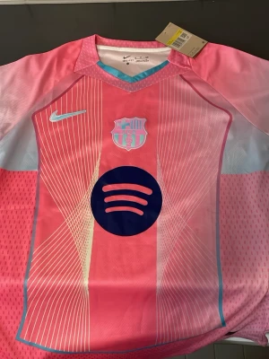 Rosa FC Barcelona Nike matchtröja - Säljer en rosa FC Barcelona matchtröja från Nike med vita och ljusblå detaljer. Tröjan har klubbmärke och Nike-logga på bröstet samt Spotify-logga i mitten. Tillverkad i lätt och ventilerande material, perfekt för träning eller match.