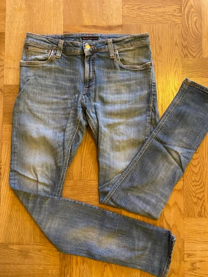 Blå slim fit jeans från Nudie - Snygga blå slim fit jeans från Nudie med klassisk femficksdesign och slitna detaljer. Jeansen har normal midja, smala ben och är gjorda i mjuk denim med stretch för extra komfort. Perfekta för en avslappnad och trendig look.