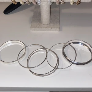 Snygga silverfärgade bangles armband - Säljer ett set med sex stilrena bangles i silverfärg. Armbanden har olika former och mönster, vissa är släta medan andra har graverade detaljer. Perfekta för att mixa och matcha för en trendig look. Materialet är metall och de är lätta att bära tillsammans eller separat.