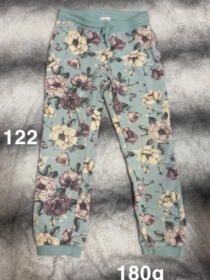 Blommiga mjukisbyxor i pastell - Snygga mjukisbyxor med ljusblå bas och stora blommor i lila, beige och vitt. Byxorna har mudd i midja och benslut samt dragsko i midjan. Perfekta för chill dagar och riktigt sköna att ha på sig.🌸 Fint använt skick. Storlek 122