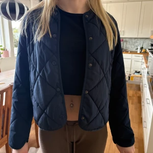 Mörkblå quiltad pufferjacka från Nelly - Snygg mörkblå vårjacka från Nelly med quiltat mönster och rund halsringning. Jackan har tryckknappar framtill. Slut på hemsidan! 