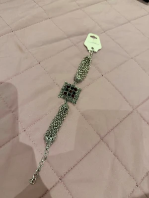 Silverfärgat armband med röda pärlor - Snyggt armband i silverfärgad metall med flera kedjor och en fyrkantig dekoration i mitten. Dekorationen har små röda pärlor som ger en cool kontrast. Perfekt accessoar för att lyfta din outfit.