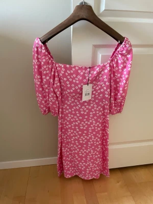 Rosa blommig klänning med puffärm - Supersöt rosa klänning med vita blommor och puffiga kortärmar. Klänningen har en rak, något figurnära passform. 