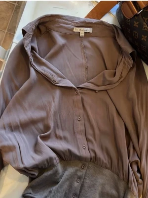 Brun blus  - Snygg brun blus från Object med knappar framtill och bred resår i midjan. Blusen har en avslappnad passform och mjukt, tunt tyg som ger ett elegant fall. Perfekt till jeans eller kjol för en trendig look.