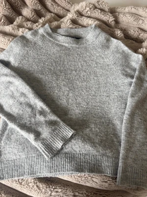 Ljusgrå stickad tröja Vero Moda - Mysig ljusgrå stickad tröja från Vero Moda med rund halsringning och ribbade muddar vid ärmslut och nederkant. Perfekt för lager på lager och enkel att matcha till olika outfits. Materialet känns mjukt och behagligt mot huden.