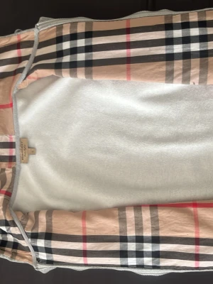 Grå hoodie från Burberry - Snygg grå hoodie från Burberry med dragkedja framtill och två fickor. Insidan har det klassiska Burberry-rutiga mönstret i beige, svart och rött. Märkets logga är broderad på bröstet. Perfekt för en chill och trendig look.