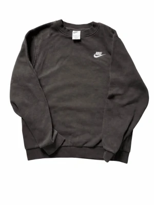 Svart sweatshirt från Nike - Klassisk svart sweatshirt från Nike med rund halsringning och vit logga broderad på bröstet. Tröjan har ribbade muddar vid ärmslut och nederkant. Perfekt för en avslappnad och sportig stil.