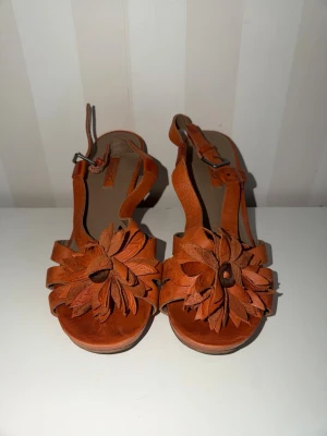 Ecco Bruna sandaler med blommor i läder - Säljer ett par bruna sandaler från Ecco i läder med öppen tå och justerbar rem runt ankeln. Sandalerna har en unik blomapplikation framtill som ger en cool och bohemisk vibe. Perfekta för dig som vill sticka ut med snygga detaljer och naturliga material.