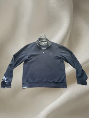 Mörkblå halvzip från Polo Ralph Lauren - Snygg mörkblå quarterzip-tröja från Polo Ralph Lauren. Tröjan har en klassisk krage med dragkedja och diskret broderad logga på bröstet. Tillverkad i mjukt bomullsmaterial som känns bekvämt mot huden. Perfekt att klä flera lager med. Väldigt mjuk och skön. 
