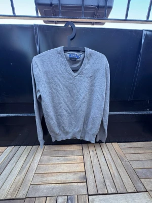 Grå V-ringad tröja Polo Ralph Lauren🙌🤩 - Klassisk grå V-ringad tröja från Polo Ralph Lauren i mjuk pima cotton. Tröjan har långa ärmar, ribbade muddar och diskret broderad logga på bröstet. Perfekt för en stilren och enkel look.🙌🤩