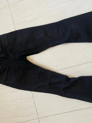 Svarta bootcut jeans - Säljer ett par svarta bootcut jeans med klassisk femficksdesign och hällor för skärp. Jeansen har en något utsvängd passform nedtill och är tillverkade i ett mjukt denimtyg som sitter snyggt på benen. Perfekta för dig som gillar en tidlös och clean look.
