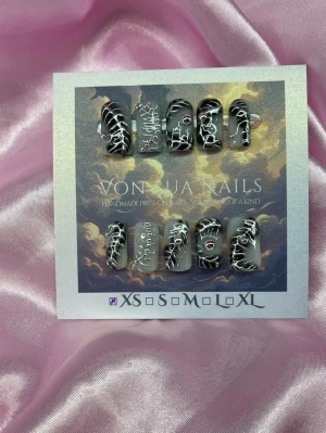 Vex (XS);Short Square;Curved - Unika handgjorda press-on naglar i svart med vita Y2K designe och små silverdetaljer. Naglarna har en kort, fyrkantig form och är handgjorda i XS: 14 mm, 11 mm, 11,5 mm, 10 mm, 8 mm . Perfekt för dig som vill ha en edgy och kreativ look.