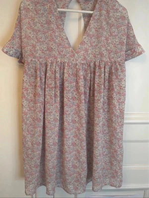 Blommig kortklänning med v-ringning - Söt kortklänning med blommigt mönster i rosa, vit och beige. Klänningen har v-ringad hals, korta ärmar och ett luftigt fall. Perfekt för varma dagar och ger en romantisk vibe.