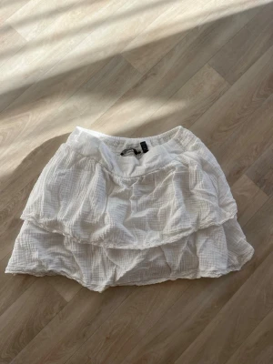 Vit volangkjol från Vero Moda - Supersöt vit kortkjol från Vero Moda med dubbla volanger och resår i midjan. Kjolen är gjord i mjuk bomull och har en lätt, luftig känsla som passar perfekt till varma dagar. Enkel att matcha med både toppar och sneakers.