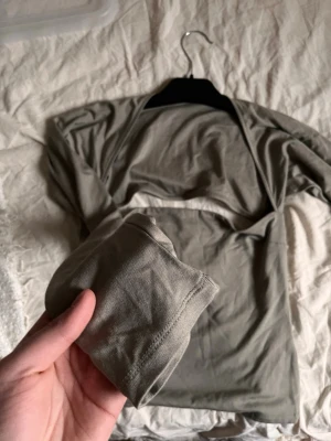 Grå långärmad croppad topp - Superfin och stilren topp som sitter riktigt snyggt på kroppen! 💕 Den är i storlek M men passar perfekt även dig som brukar ha S, då den är stretchig och formar sig efter kroppen.  Det bästa med toppen är den lite öppna ryggen som ger en extra snygg och feminin touch – perfekt både till vardag och fest.  ✔ Figurnära passform ✔ Bekväm och stretchig ✔ Trendig öppen rygg ✔ Lätt att matcha  Säljes i fint skick! 🌸 
