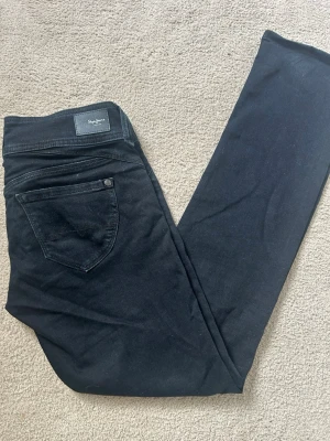 Svarta jeans från Pepe Jeans - Säljer ett par svarta mid waist straight jeans från Pepe Jeans med klassisk femficksdesign och diskret logga bak i midjan. Perfekta för en stilren och enkel look.