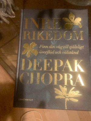 Inre rikedom av Deepak Chopra - En inspirerande bok med hård pärm i mörkblått och guld, skriven av Deepak Chopra. Omslaget har guldfärgade blommor och text. Boken handlar om att hitta själsligt överflöd och välstånd genom meditation och mindfulness. Perfekt för dig som vill utvecklas personligt.