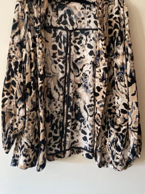 Leopardmönstrad öppen kofta - Säljer en luftig och mjuk öppen kofta med leopardmönster i beige, svart och bruna toner. Koftan har långa ärmar och ett avslappnat fall, perfekt för att lyfta vilken outfit som helst. Materialet känns stretchigt och bekvämt.