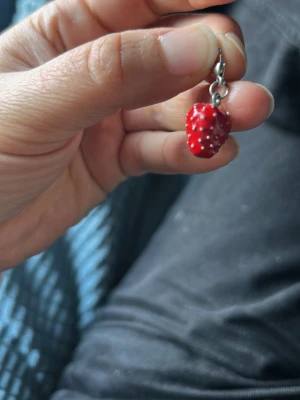 Jordgubb berlock - Sött berlock  format som en jordgubbe i röd med vita prickar och grön topp. Hängsmycket har en metallkrok i silverfärg. Perfekt för dig som gillar lekfulla accessoarer och vill sticka ut lite extra.