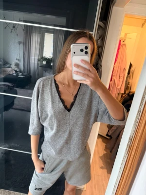 Grå tröja med spetsdetalj - Mysig grå tröja i mjukt material och V-ringning dekorerad med svart spets. Trekvartsärmar med avslappnad passform. Perfekt för chill hemma eller slappa dagar.
