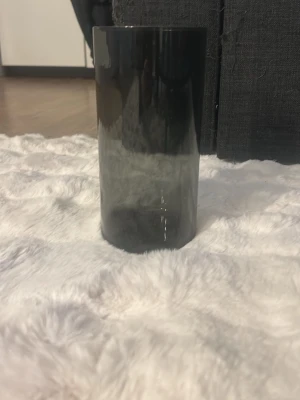 Cylindrisk grå plastvas - Snygg cylindrisk vas i gråtonat plast. Perfekt för snittblommor eller som dekoration på bordet. Glaset har en mjuk övergång från mörkare till ljusare grå och en stilren, minimalistisk design som passar i de flesta hem.