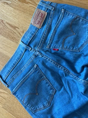 Blå Levi's skinny jeans - Säljer ett par klassiska blå skinny jeans från Levi's med fem fickor och den ikoniska röda Levi's-lappen bak. Jeansen har normal midja och smal passform hela vägen ner. Perfekta till vardags och lätta att matcha med allt. 1