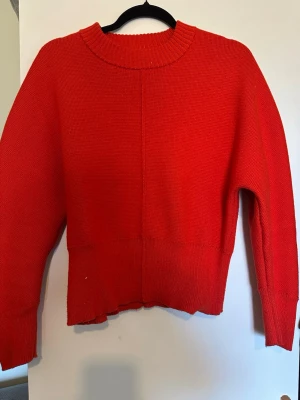 Röd stickad tröja med ribbad kant - Snygg röd stickad tröja med rund halsringning och ribbade muddar. Tröjan har en rak passform och är något croppad i modellen. Perfekt att matcha med jeans för en avslappnad look.
