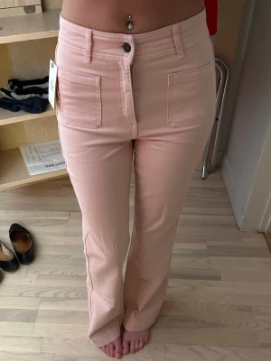 Ljusrosa jeans från H&M - Säljer ett par ljusrosa jeans från H&M med regular midja och bootcut passform. Jeansen har stora framfickor och bälteshällor, samt en knapp och dragkedja framtill. Perfekta för dig som vill ha en trendig och bekväm look. Helt nya också