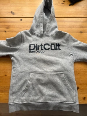 Grå Dirtcult Hoodie  - Grå Dirtcult Hoodie med svart tryck i storlek 158/164 lite sliten i armarna och trycket men håller ändå.